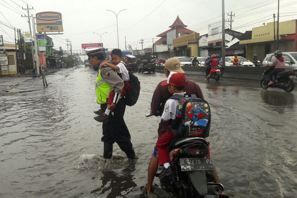 Anggota Satlantas Polsek Genuk menggendong anak sekolah untuk menyeberangi jalan yang tergenang banjir, Senin (29/1). (Foto: Polrestabes Semarang, Jateng).
