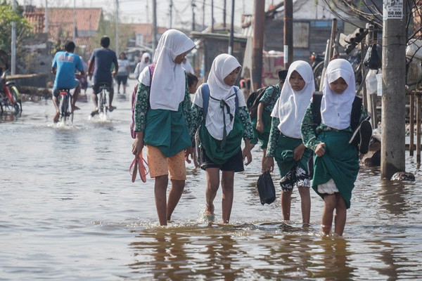 Para siswi terpaksa tak mengenakan sepatu dan mengangkat seragam saat melintasi jalan yang tergenang rob di Kota Pekalongan, Jateng, 24 Mei 2018. (Foto: Antara Foto/Harviyan PP)