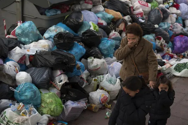 Ilustrasi seorang ibu dan dua anaknya menutup hidung saat melintasi tumpukan sampah berbau busuk. (Foto: AP/Laura Leon)
