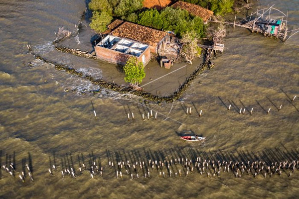 Perahu nelayan melintas di antara struktur konstruksi pasak hybrid engineering dan rumah yang rusak akibat abrasi di pesisir Sayung, Kabupaten Demak, Jateng, Kamis (7/11). (Foto: Antara Foto/Aji Styawan)
