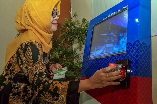 Seorang pedagang tengah mengetap kartu di mesin retribusi-el pasar. (Foto: Pemkot Surakarta)
